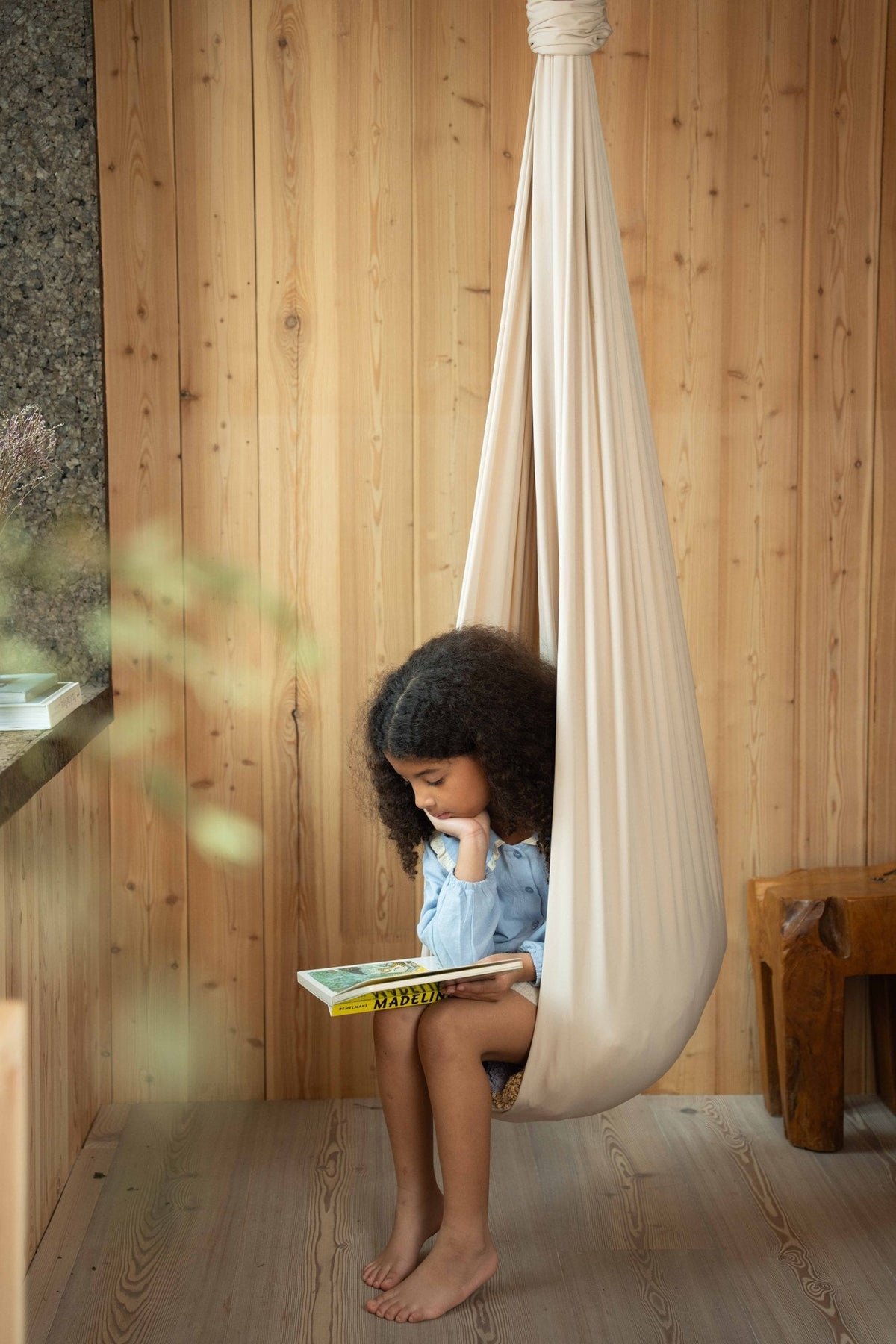 A child reading in a cream Saint Esen sensory swing beside a window