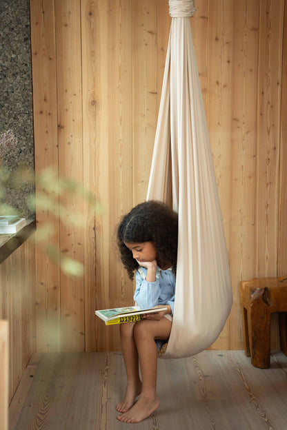 A child reading in a cream Saint Esen sensory swing beside a window