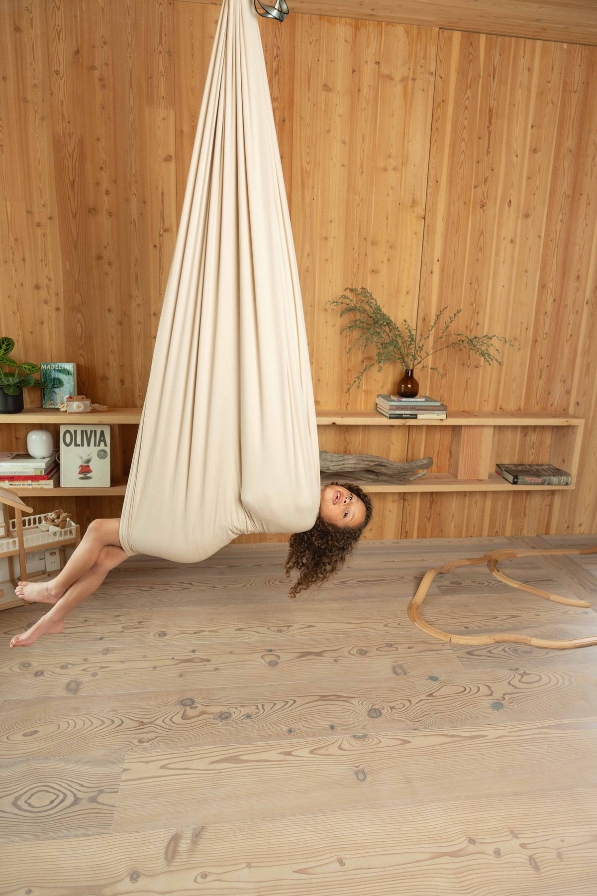 A child lying flat inside a cream sensory swing, the fabric closed over her