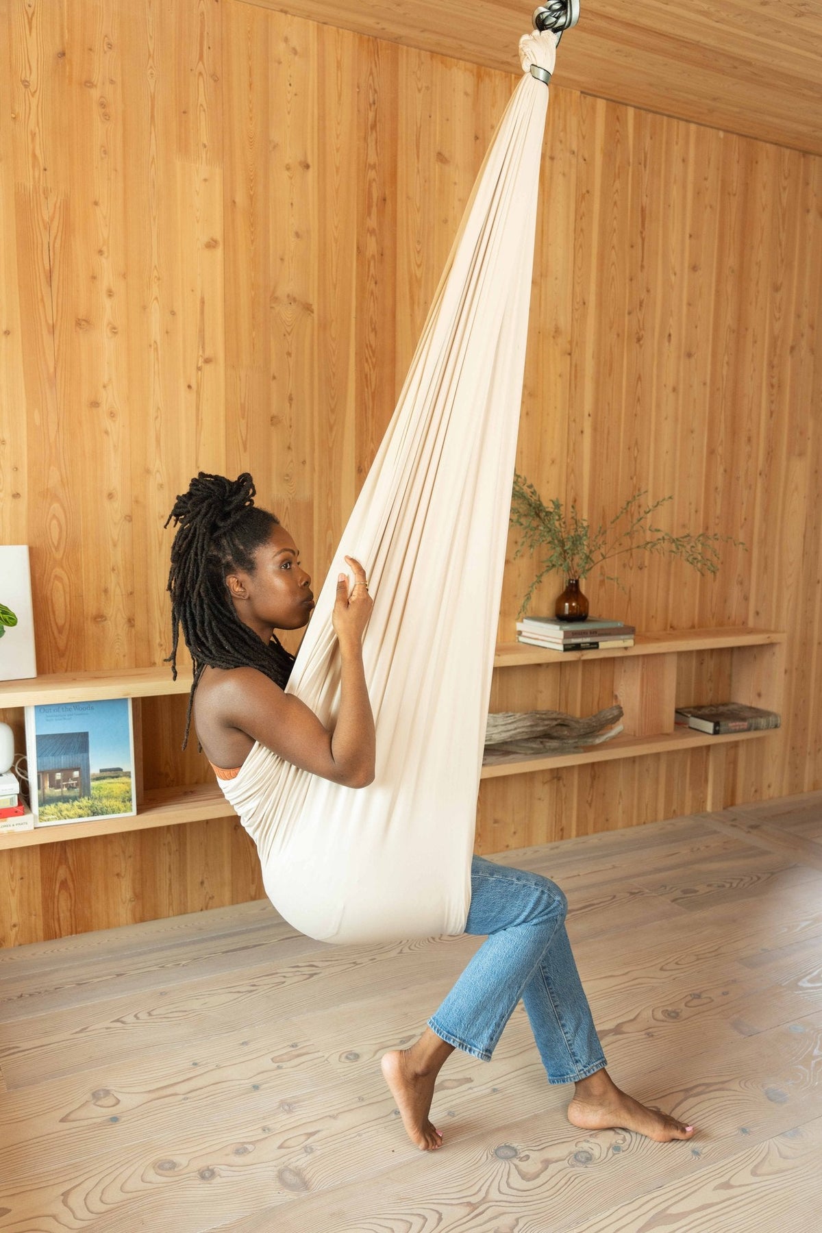 An adult sitting sideways in a cream sensory swing, feet on the floor, in a wood paneled room