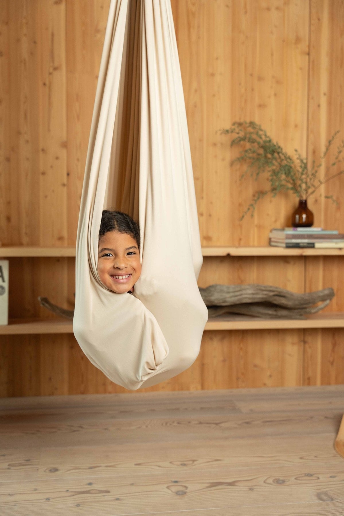 A child peeking out of a fully cocooned cream sensory swing