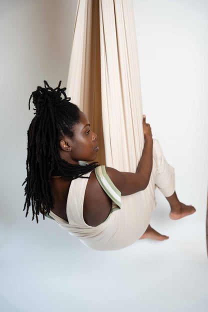 An adult sitting in a cream sensory swing against a white background