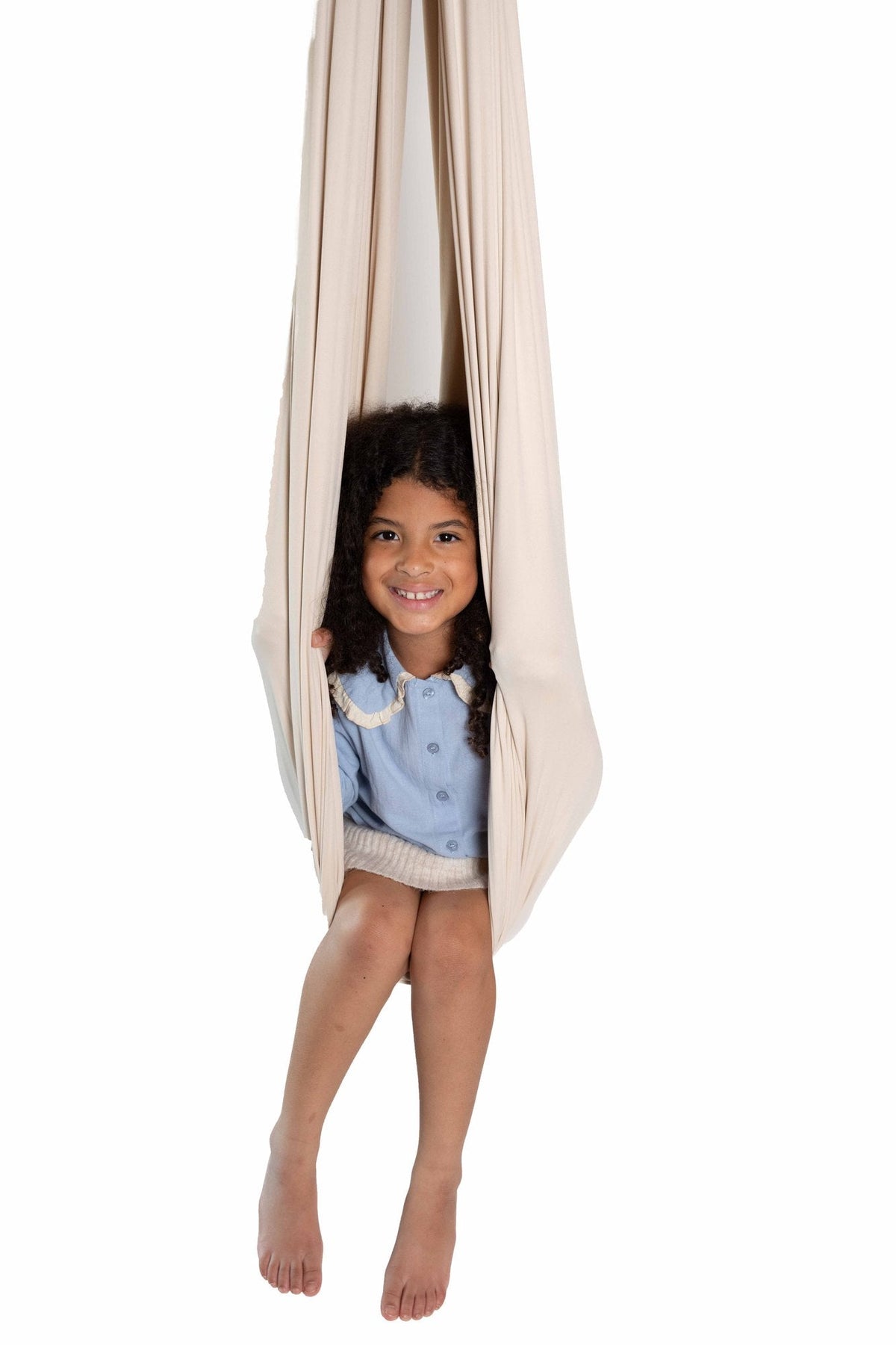 A smiling child sitting in a cream sensory swing against a white background